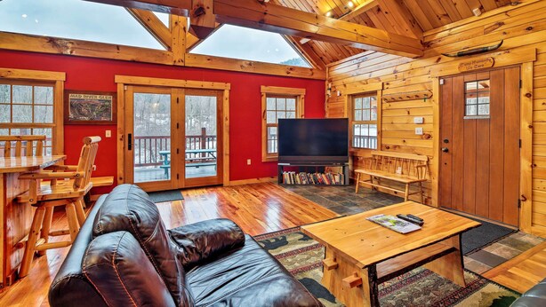 A spacious cabin with a large living area, wooden walls, a red accent wall, a fireplace, and a television. - Ski Lodge Mtn Retreat w/ Fire Pit, Deck & Views! (Starksboro)