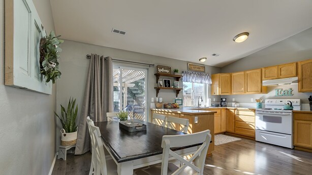 Una cocina con armarios de madera, estufa blanca y una mesa de comedor con sillas blancas.