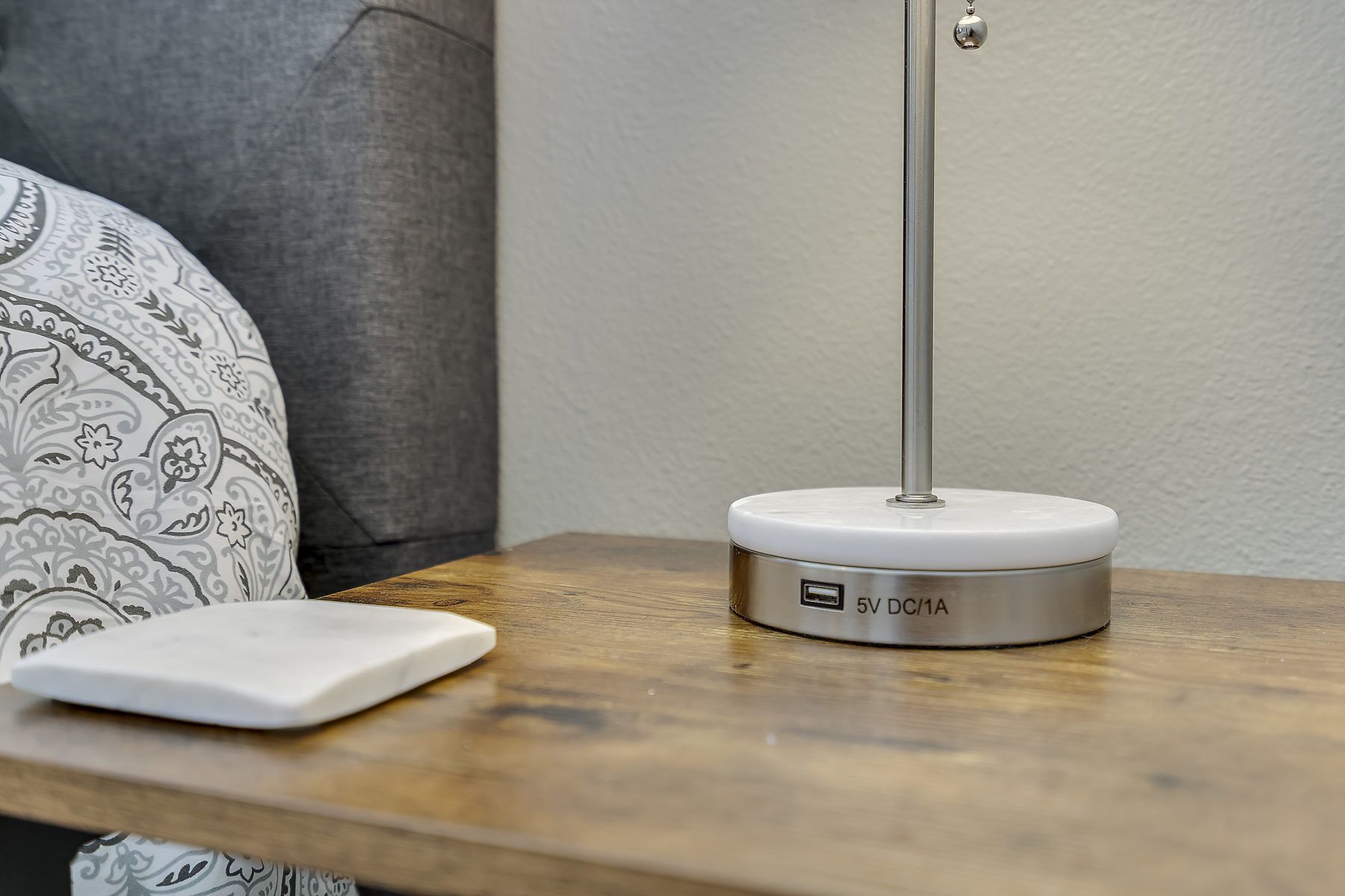 Une table de chevet avec une lampe blanche et un chargeur blanc.