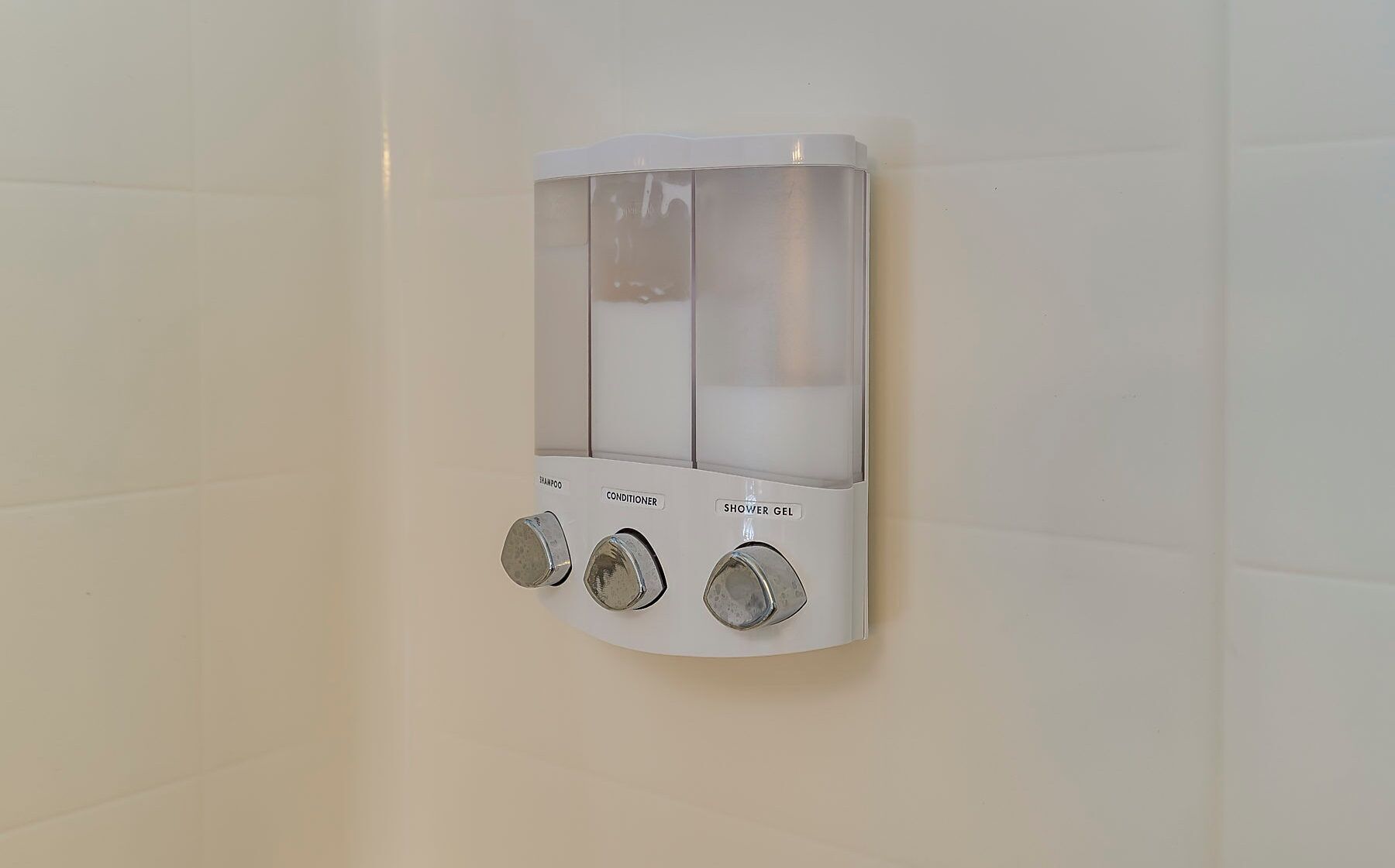 En vægmonteret dispenser med tre rum til shampoo, balsam og brusegel.