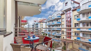 Un balcon agrémenté de chaises en osier et d’une petite table, d’où l’on peut admirer une rangée d’immeubles à plusieurs étages, chacun doté d’un balcon.
