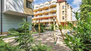 Un immeuble à plusieurs étages doté de balcons, une aire de jeux avec des balançoires et de nombreux espaces verts environnants.
