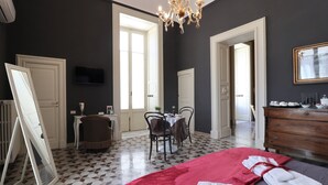 A hotel room with a large bed, a red blanket, a TV, a chandelier, a dining area with chairs and a table, and a dresser. - Chez Moi Lecce Charme B&B (Lecce)