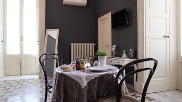 Un comedor con una mesa puesta para dos, un radiador, un televisor montado en la pared y una puerta que da a otra habitación.