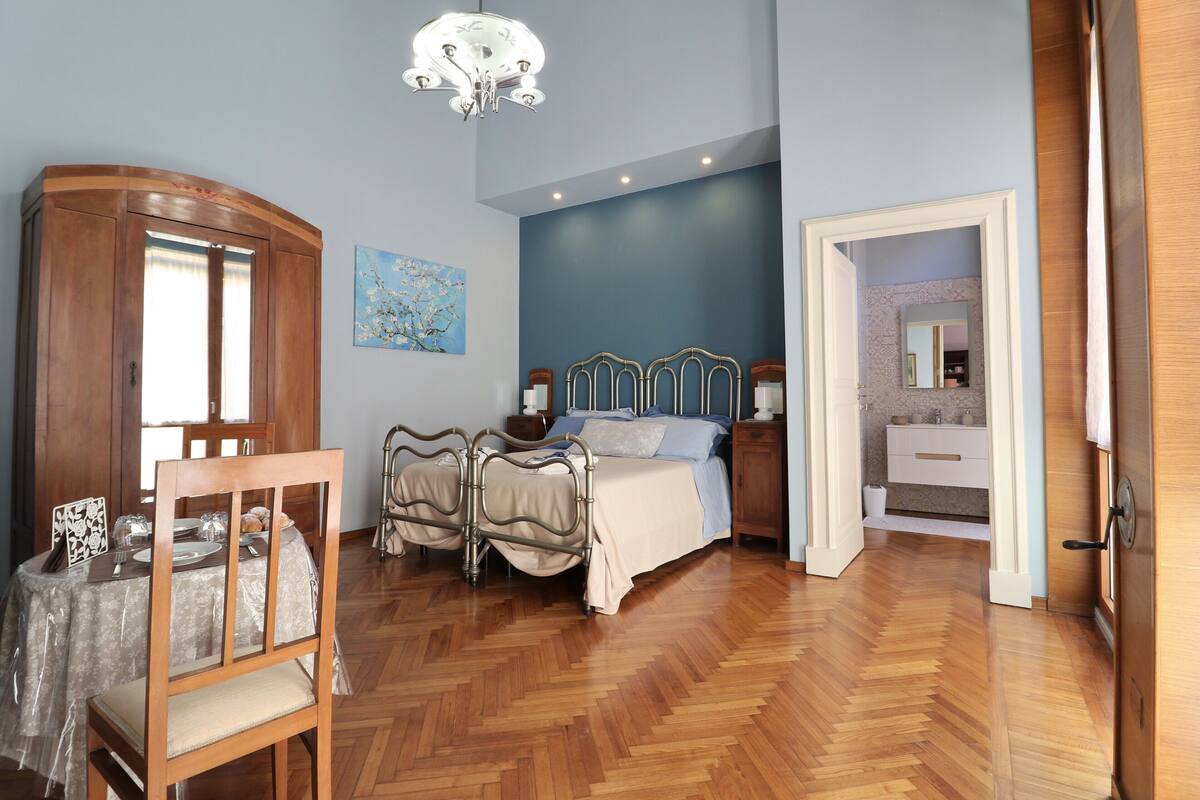 A bedroom with a wooden floor, a bed with a headboard, a nightstand, and a chair.