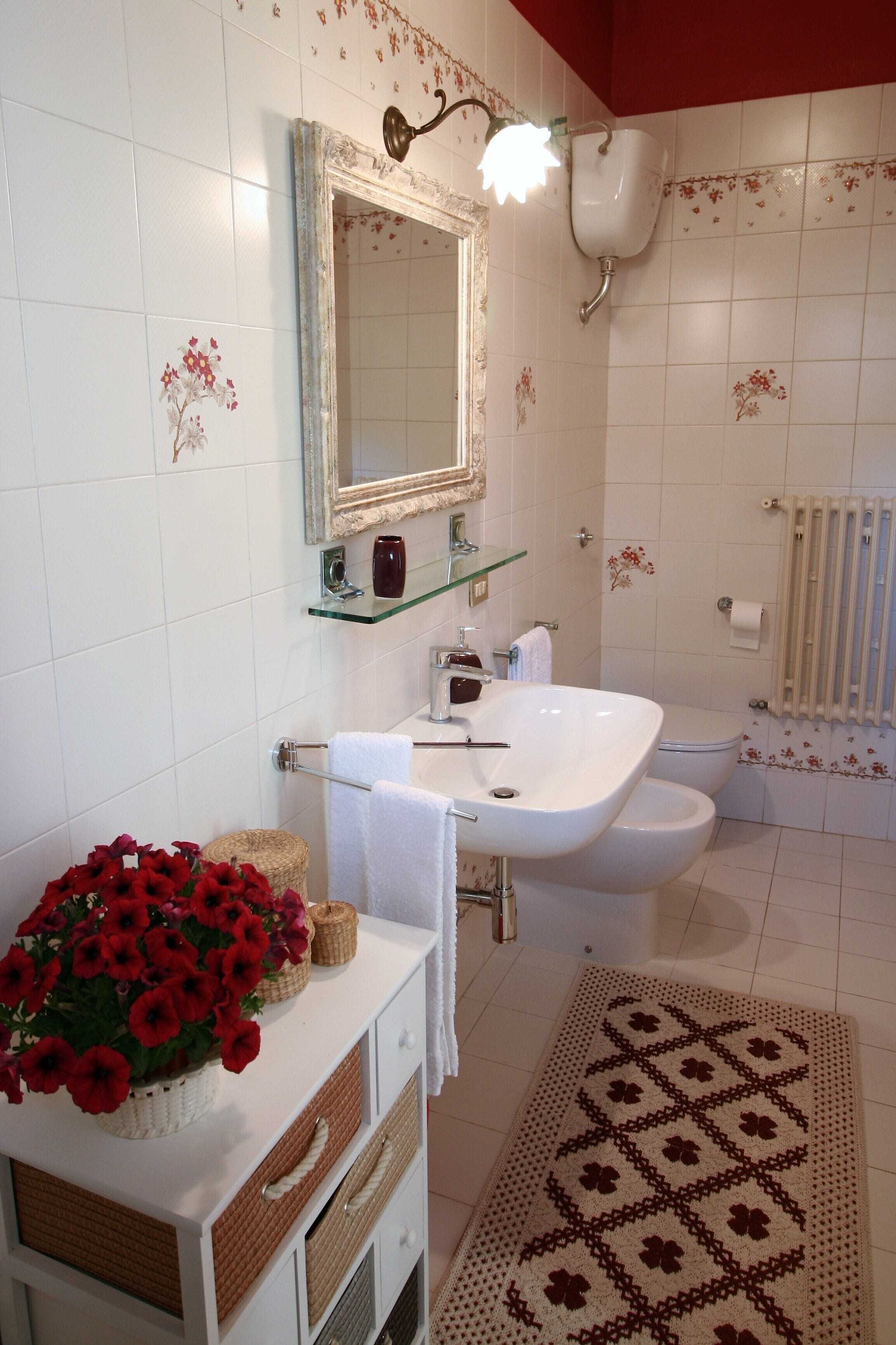 A bathroom with a white sink, a glass shelf, a mirror, and a patterned rug.