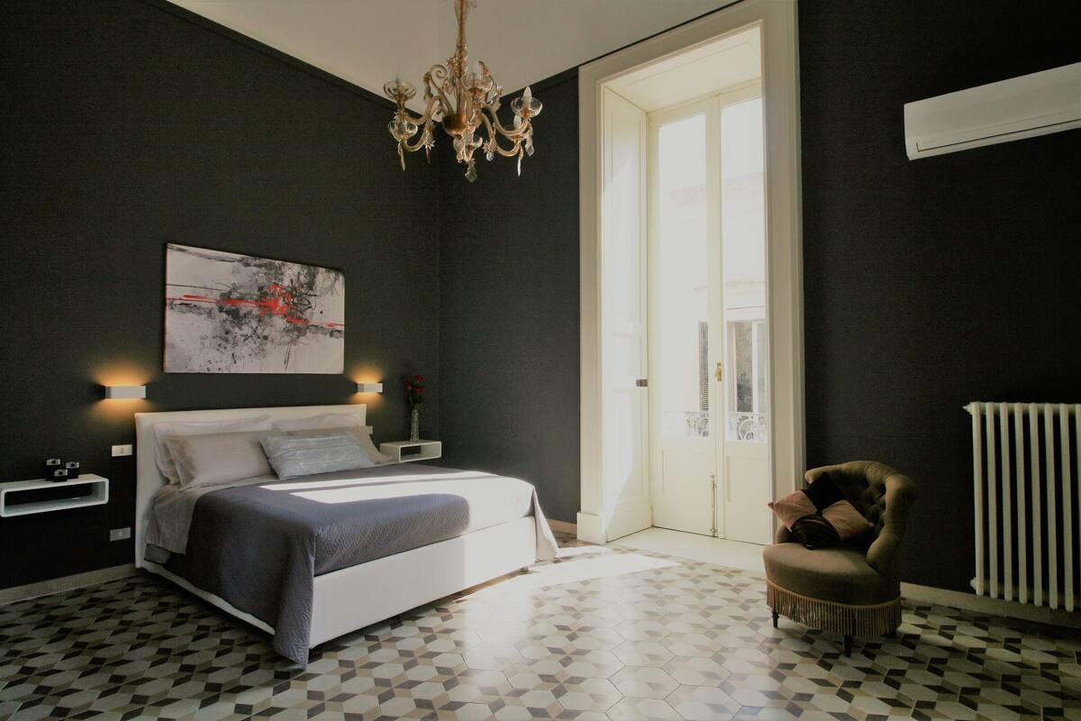 A modern bedroom with a bed, bedside tables, a chandelier, a chair, and a radiator.