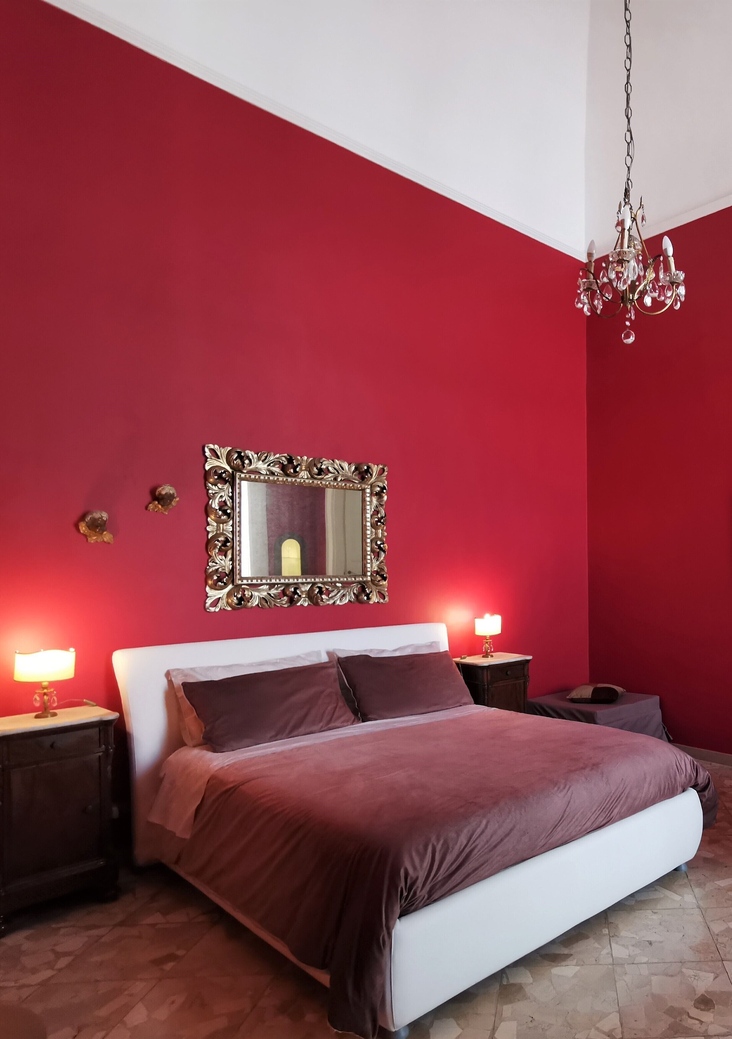 Een slaapkamer met een wit bed, rode muren, een kroonluchter en bedlampjes.