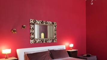 Een slaapkamer met een wit bed, rode muren, een kroonluchter en bedlampjes.