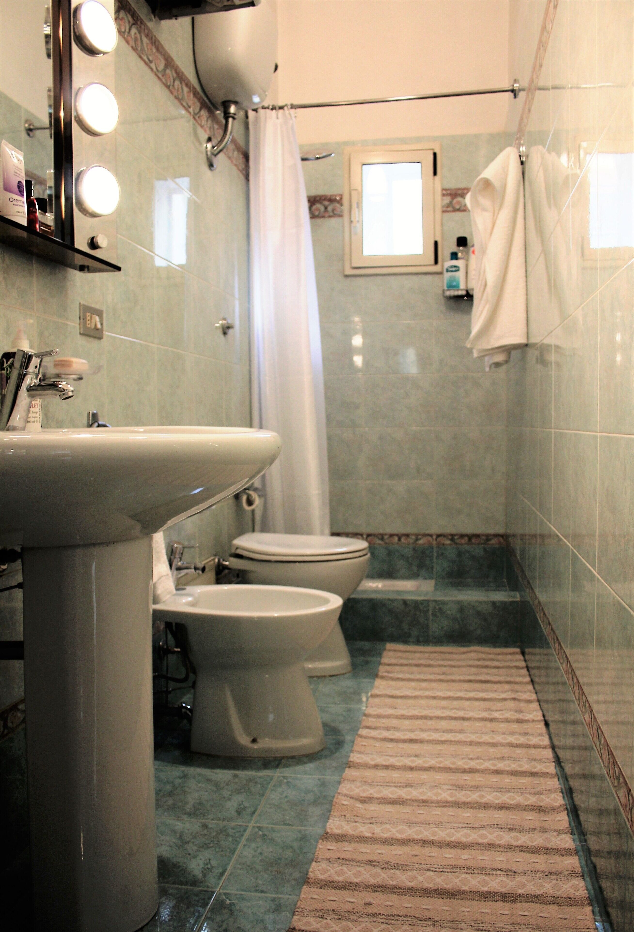 A bathroom with a sink, two toilets, a shower curtain, and a towel rack.