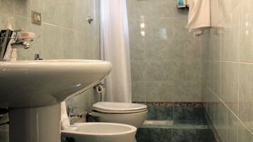 A bathroom with a sink, two toilets, a shower curtain, and a towel rack.
