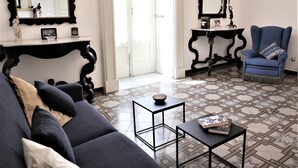 A living room with a sofa, armchairs, a coffee table, and two side tables. There are two large mirrors on the walls, a door leading to another room, and a patterned floor. - Chez Moi Lecce Charme B&B (Lecce)