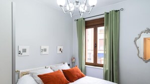 Une chambre à coucher avec un lit, un lustre, une fenêtre avec des rideaux et des œuvres d’art murales.