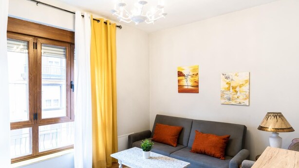Un salon moderne avec un canapé gris, une table basse blanche et un rideau jaune.