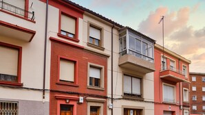 Une rangée d’immeubles résidentiels à plusieurs étages, dotés de balcons, avec une rue devant et des voitures garées.