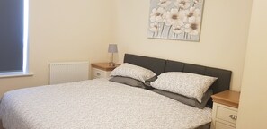 A bedroom with a bed, a nightstand, a lamp, a radiator, and a wall art piece.
