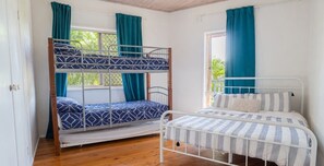 A room with a bunk bed and a single bed, both with metal frames, and a window with curtains. - Ocean Views Sleeps 20 (Fraser Island)