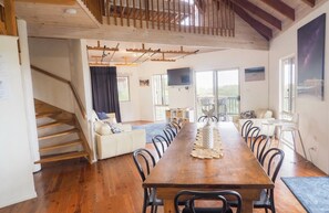 A dining area with a long wooden table, multiple chairs, a sofa, and a staircase leading to another room.