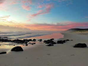 A beach with sand, rocks, and a calm sea under a sunset sky. - Ocean Views Sleeps 20 (Fraser Island)