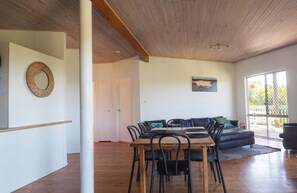 A dining area with a wooden table and chairs, a black sofa, and a large window with a view. - Ocean Views Sleeps 20 (Fraser Island)