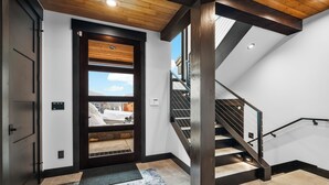 A modern interior with a wooden staircase, a door with a view to the outside, and a textured rug on the floor. - Ski-in/Ski-Out Luxury Schweitzer•Hot Tub•4 King Suites•Walk to Village•Ski Room (Sandpoint)