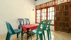 A dining area with a table covered in a red tablecloth, surrounded by four green plastic chairs. A wooden door with glass panels is visible in the background. - JIO Homestay (Yogyakarta)
