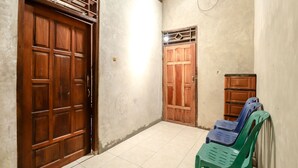 A corridor with two wooden doors, a tiled floor, and a green plastic chair. - JIO Homestay (Yogyakarta)