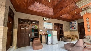 A cozy room with a wooden ceiling, a refrigerator, a water dispenser, a sofa, and a bench. - Padi-Padi Hostel & Bar (Ubud)
