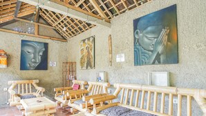 A room with bamboo furniture, including sofas and a table, with a large Buddha painting on the wall. - Padi-Padi Hostel & Bar (Ubud)