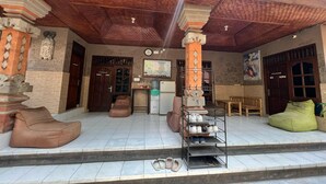 A covered outdoor area with a tiled floor, a refrigerator, a bench, and a shoe rack. - Padi-Padi Hostel & Bar (Ubud)