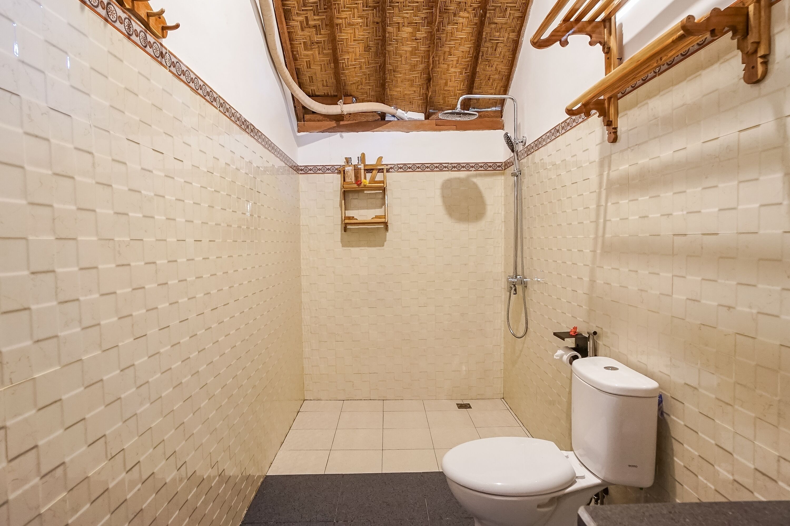 A small, tiled bathroom with a toilet, shower, and a shelf with toiletries.