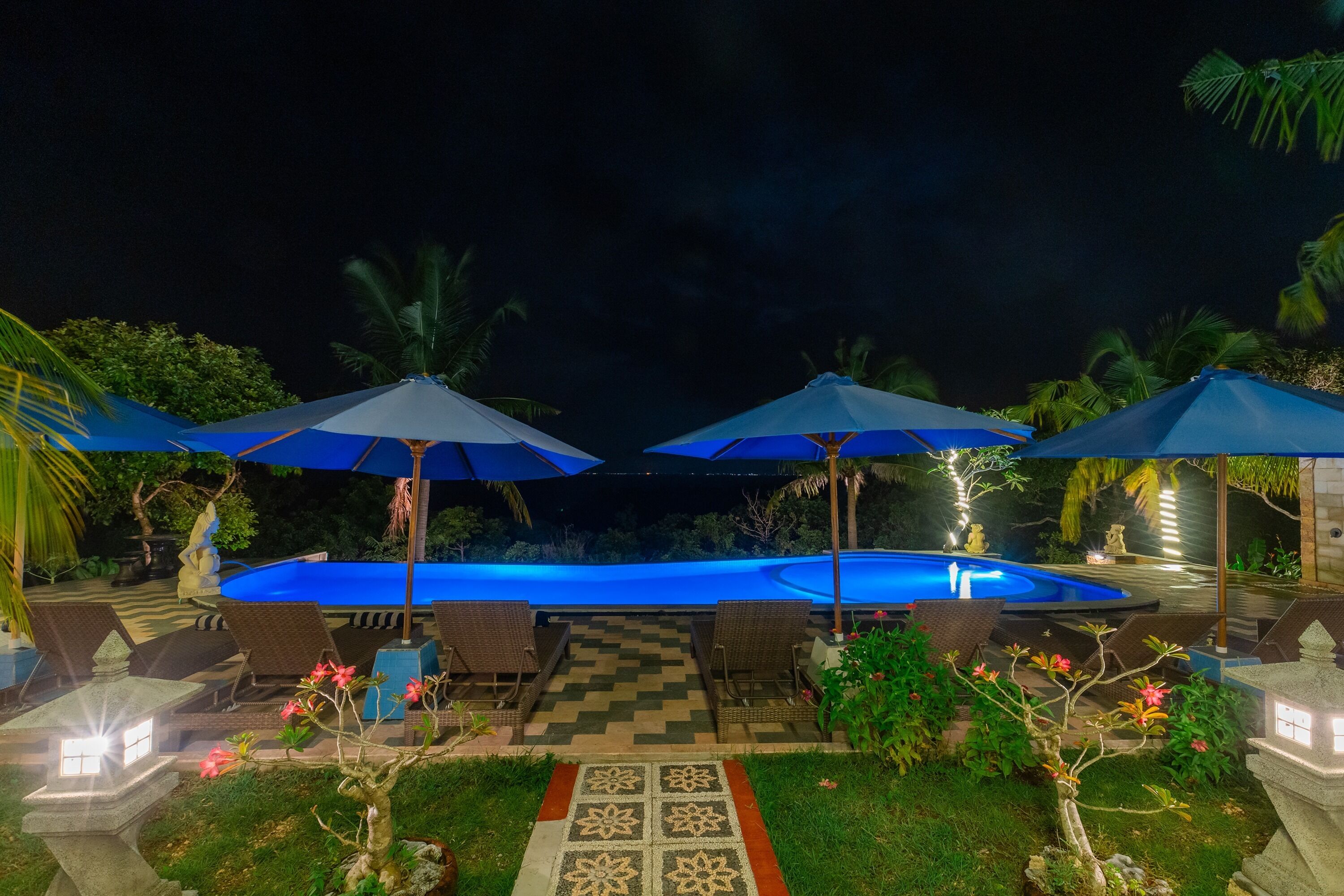 A pool area with lounge chairs and umbrellas, surrounded by greenery and decorative elements.