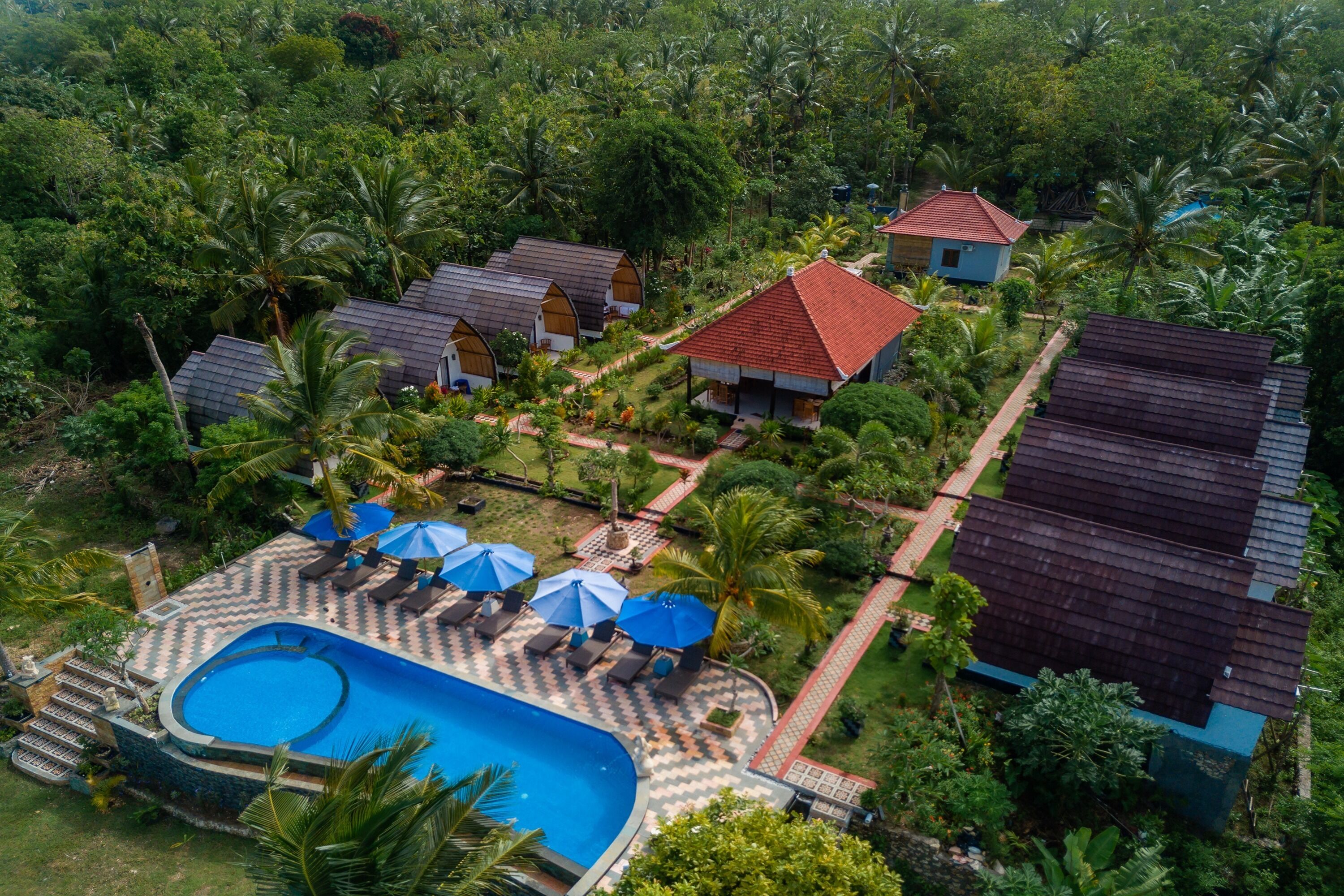 Vue aérienne d’un complexe hôtelier avec une piscine, des chaises longues et un jardin tropical.