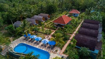 Vue aérienne d’un complexe hôtelier avec une piscine, des chaises longues et un jardin tropical.