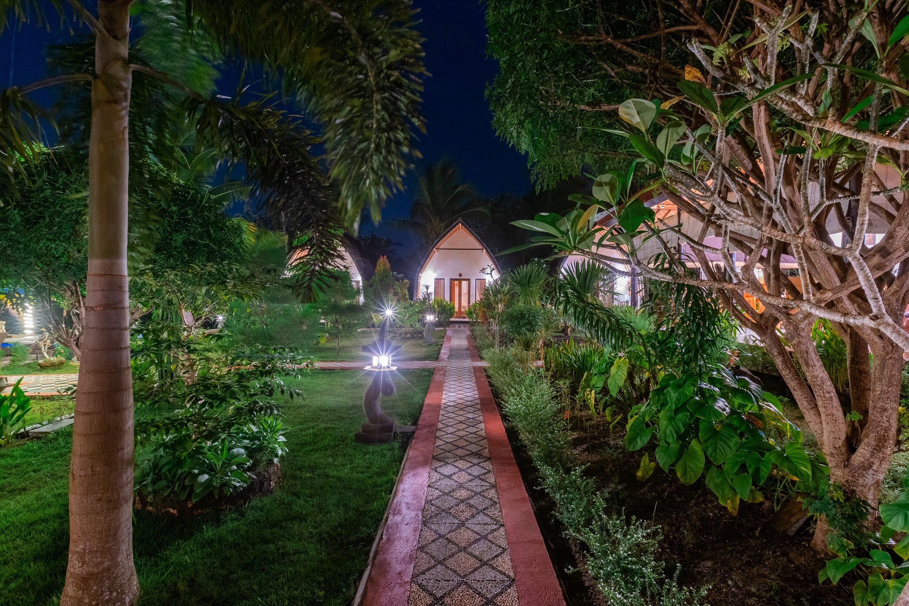 Un sendero conduce a un edificio rodeado de abundante vegetación y palmeras.