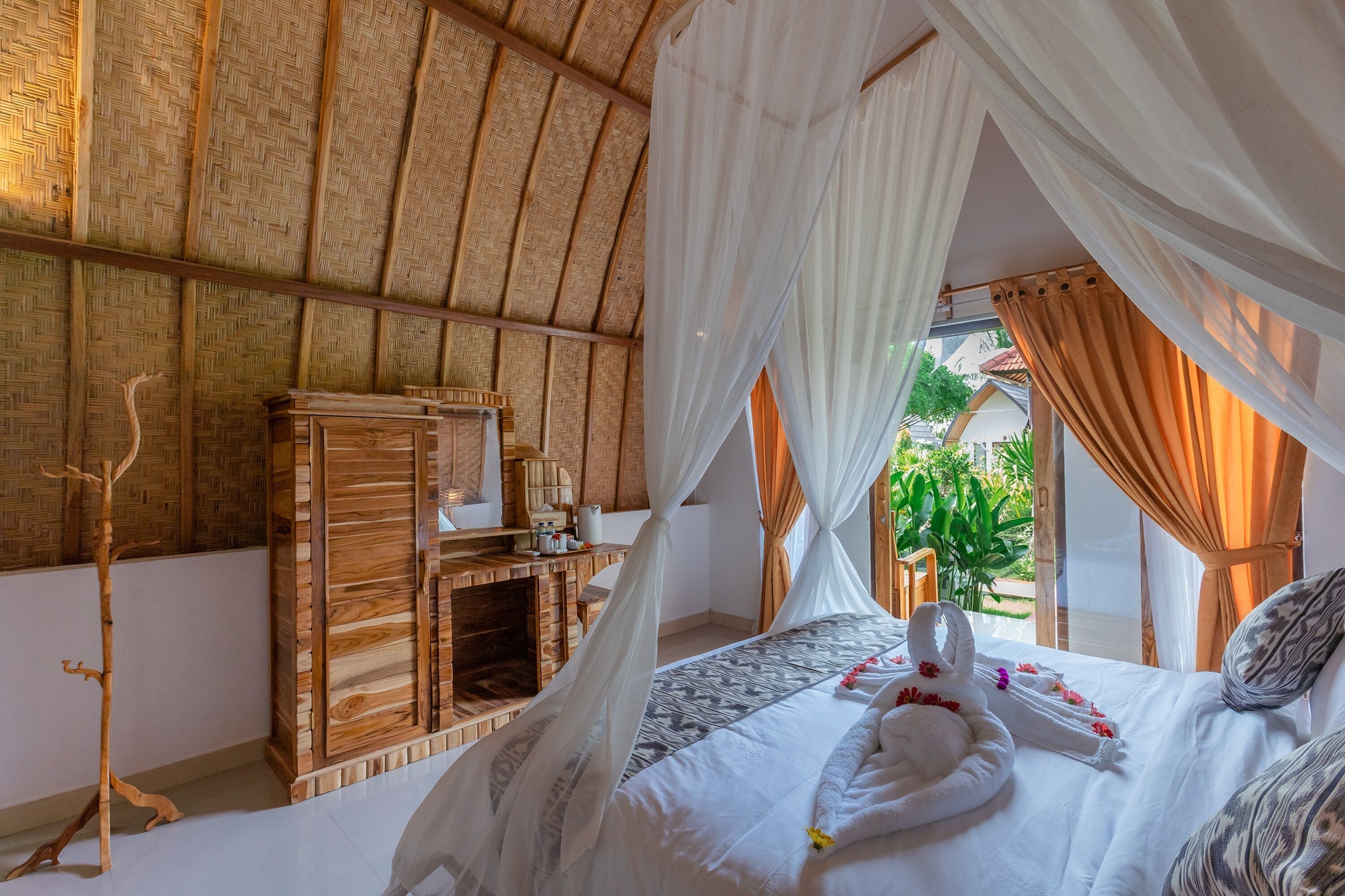 A room with a bed, a wooden cabinet, and a view of greenery outside.