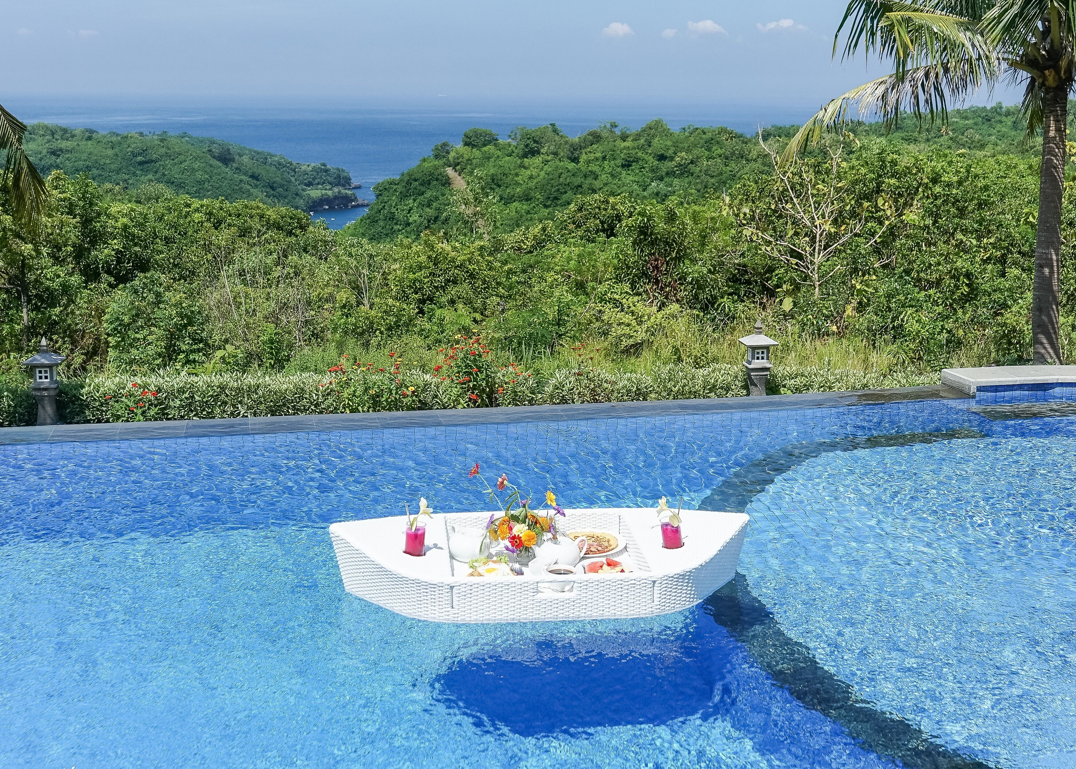 Une piscine dotée d’un bar flottant, entourée d’une végétation luxuriante et offrant une vue sur l’océan.