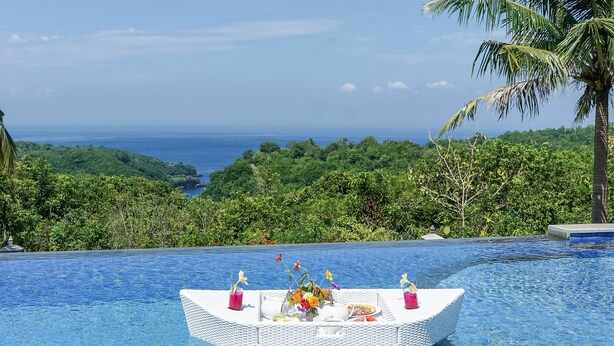 Un área de comedor flotante en una piscina, con vista al océano y abundante vegetación.