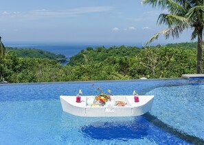 Un área de comedor flotante en una piscina, con vista al océano y abundante vegetación.