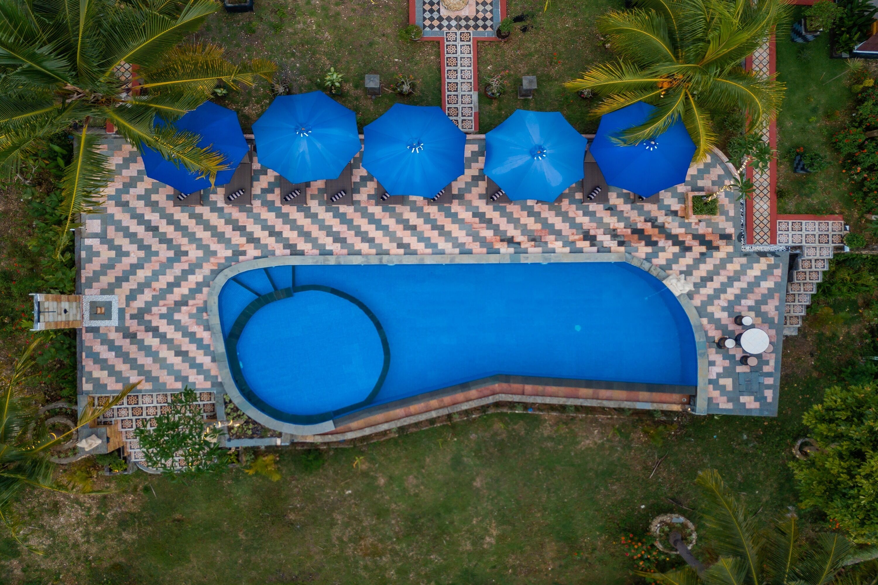 An aerial view of a swimming pool with blue umbrellas and checkered flooring.