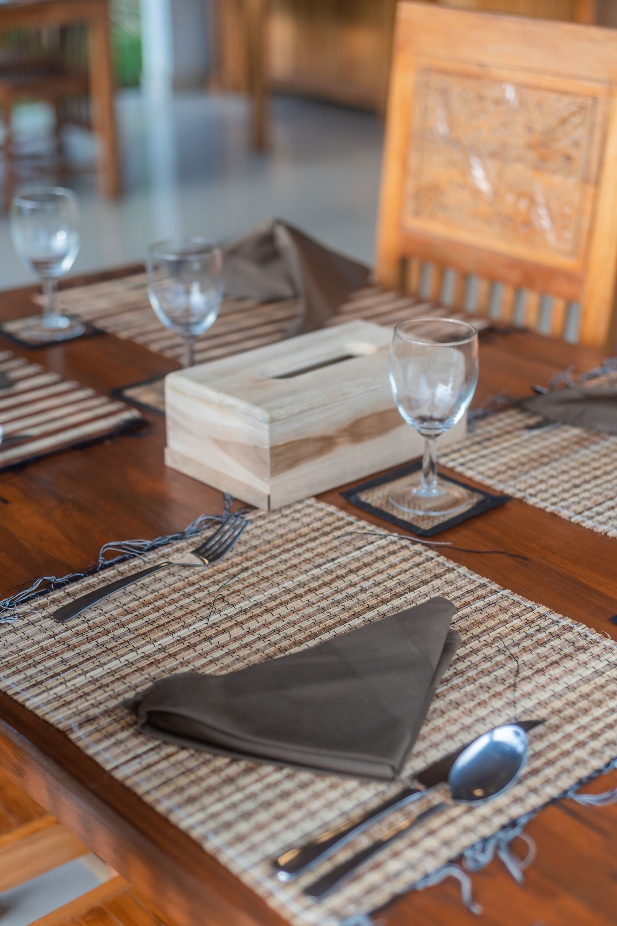 Une table de salle à manger en bois, mise avec des sets de table, des couverts, un verre et une serviette.