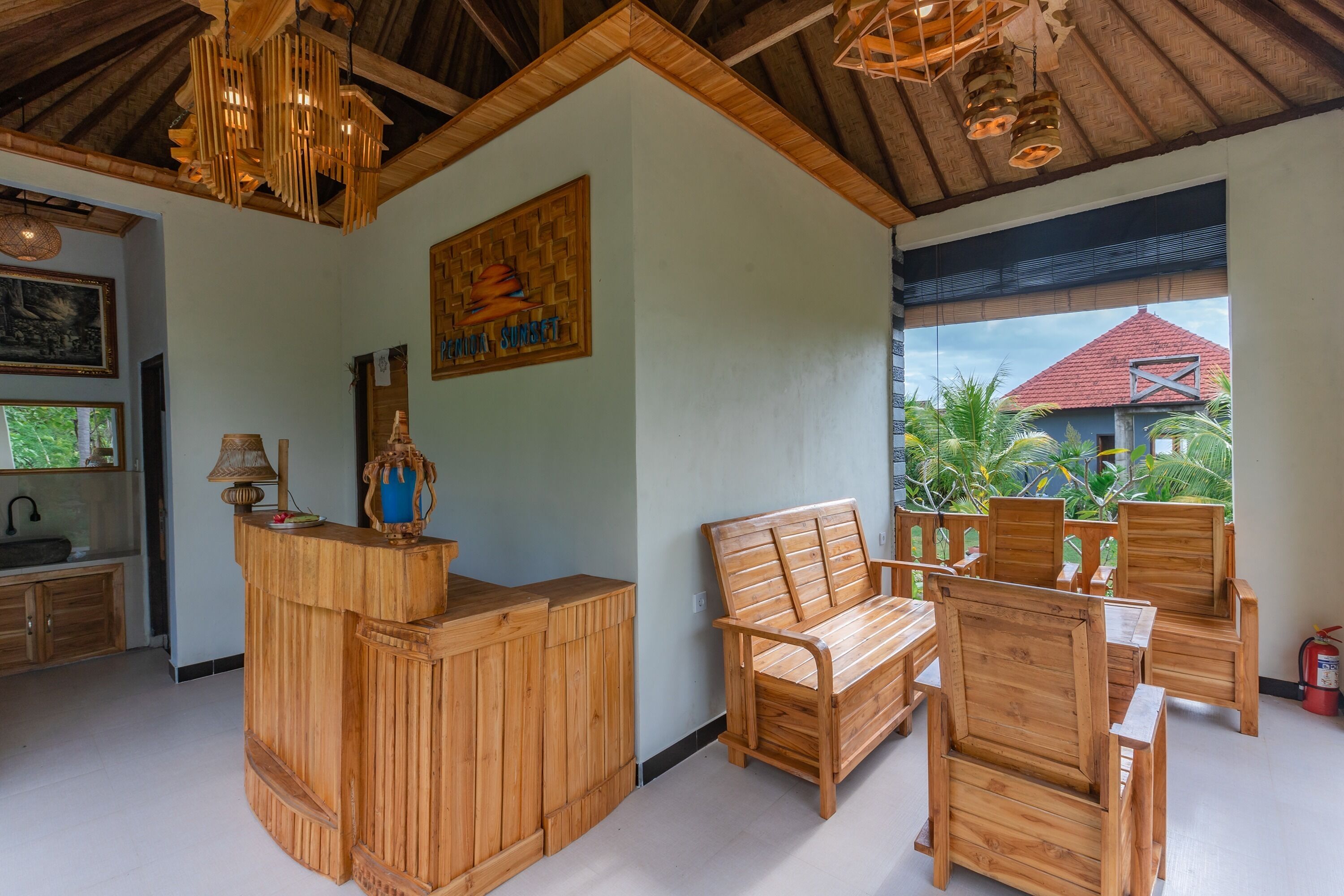 A wooden reception desk, a wooden bench, and several wooden chairs in a room with a high ceiling and a view of the outside.