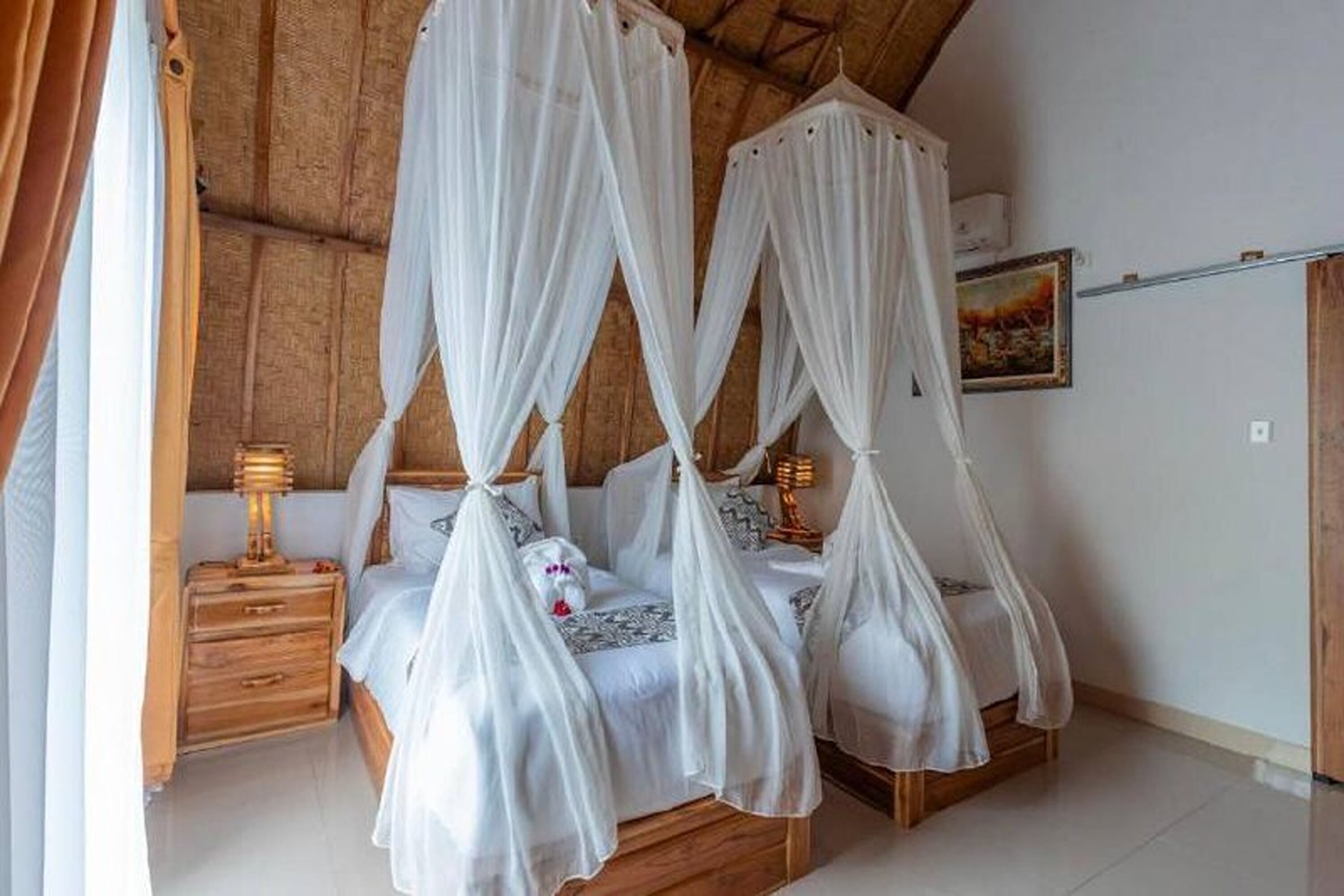 Ein Bett mit Baldachin, weißem Moskitonetz, einem Holzkopfteil und Nachttischen mit Lampen.