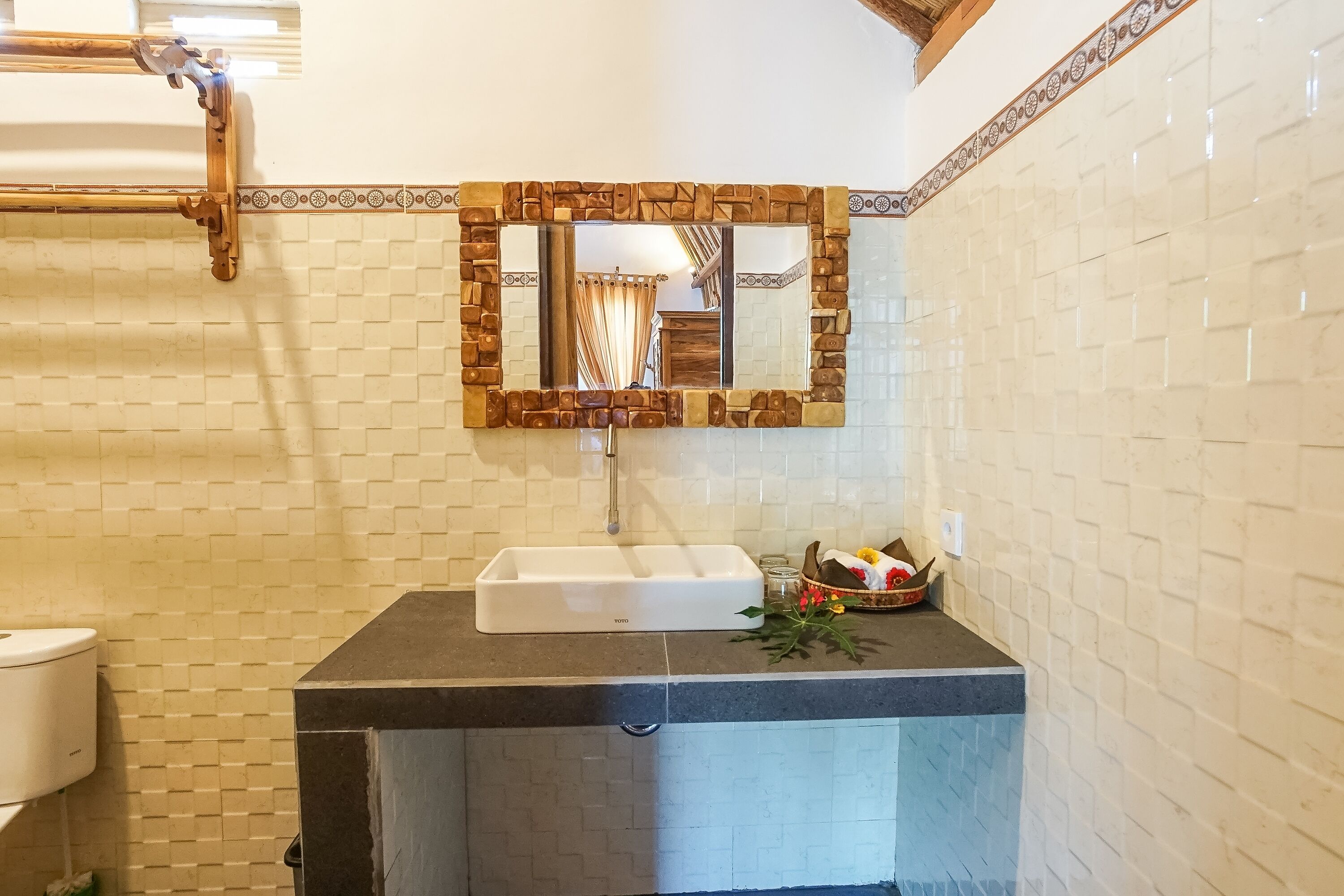 Un bagno con un lavandino bianco, uno specchio con cornice in legno e una parete rivestita di piastrelle.