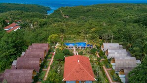 Vista aérea de un resort con múltiples alojamientos tipo cabaña, una piscina central y exuberante vegetación circundante.