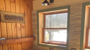 A kitchen with wooden cabinets, a stone backsplash, a window with a view of trees, and a 'FAMILY' sign on the wall.