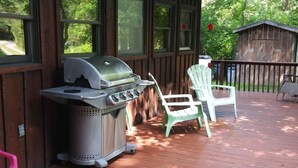 A covered outdoor area with a grill, two Adirondack chairs, and a wooden deck.