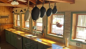 A kitchen with wooden cabinets, a bar area, hanging pots, and a stone wall.