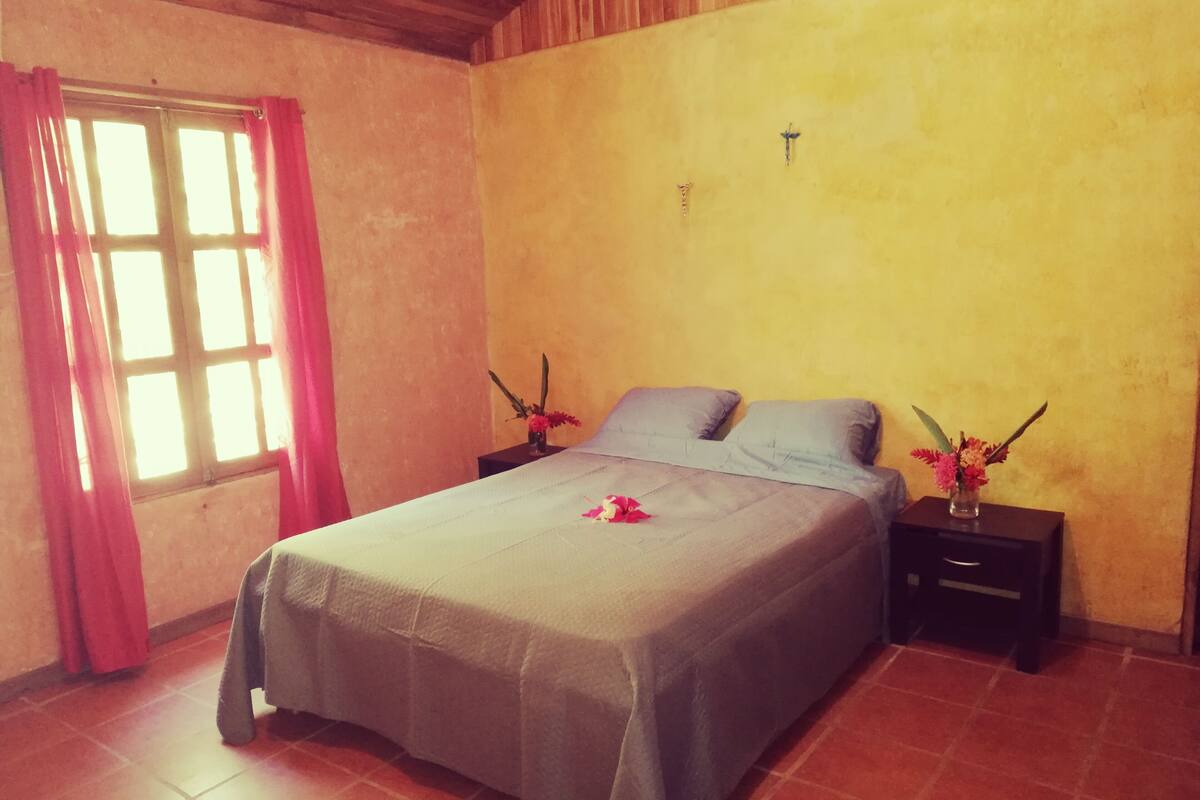 A bedroom with a bed, curtains, a nightstand, and a wall-mounted light.