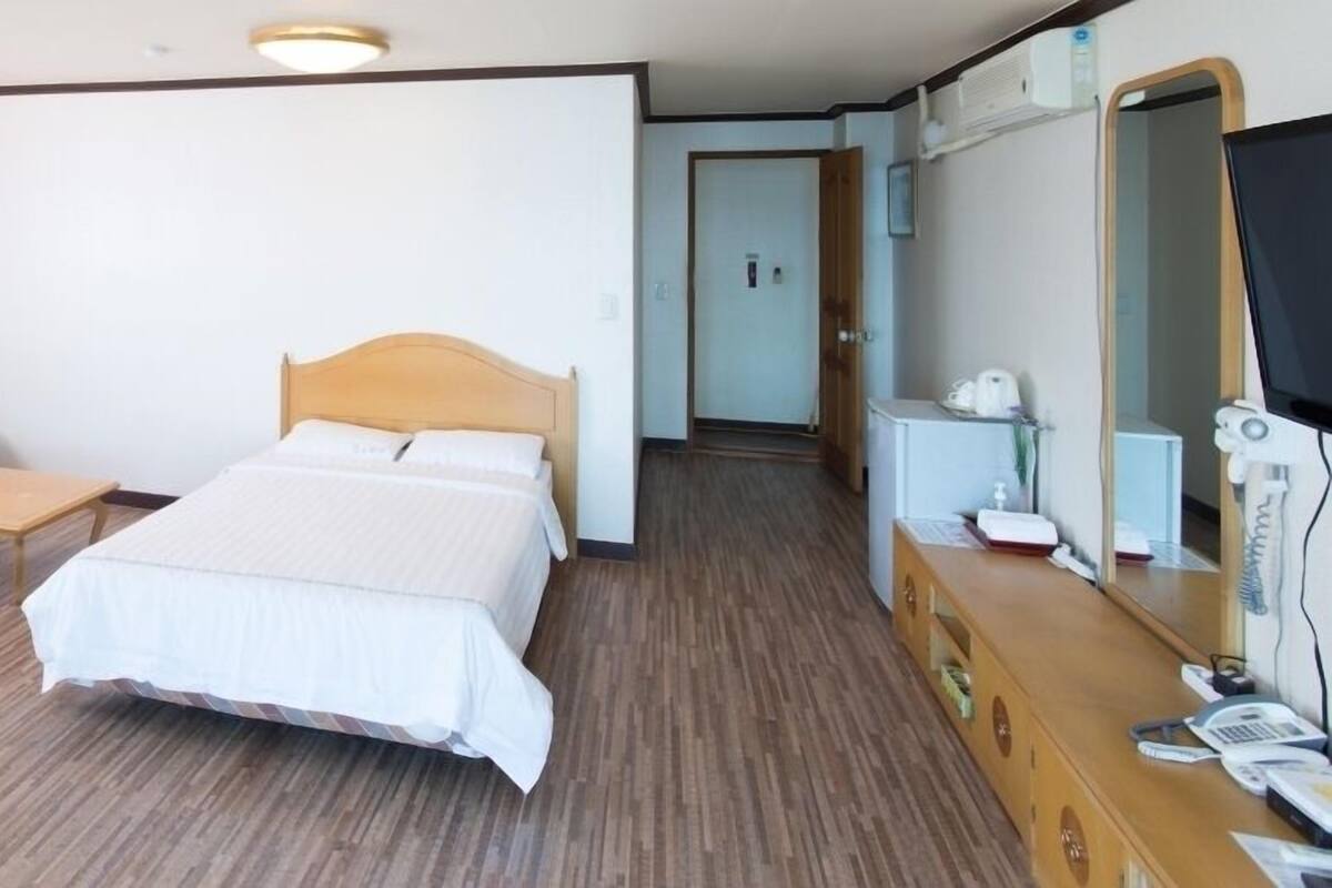 A hotel room with a bed, a sofa, a small table, a dresser with a mirror, and a television.